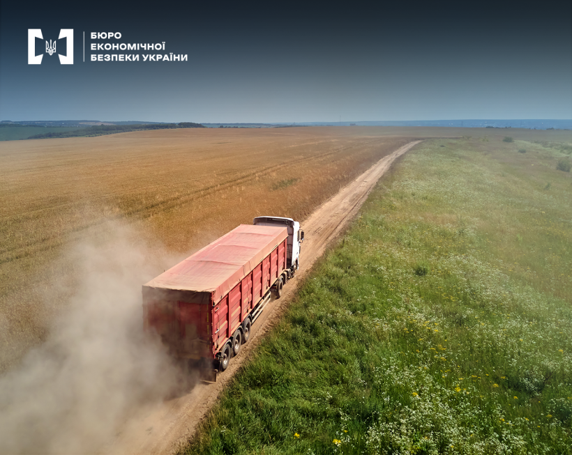 Вигляд зверху. Фура з червоним тентом їде ґрунтовою дорогою поміж полів, здіймаючи за собою пил.