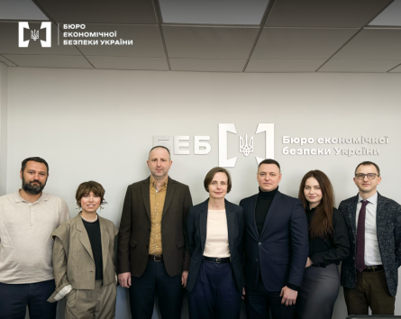 A group photo of representatives of the Economic Security Bureau of Ukraine  against the backdrop of the department's official logo during a working meeting or conference.