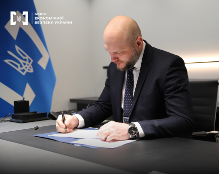 Директор БЕБ Олександр Цивінський підписує документи на фоні відомчого прапора.