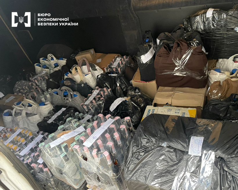 Темне складське приміщення заповнене великою кількістю пакетів, коробок та мішків з контрафактним алкоголем в різних тарах.