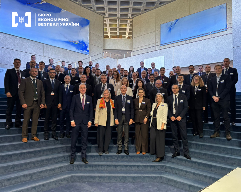 Participants of an international meeting posing for a group photo on the stairs. Everyone is dressed in business attire.
