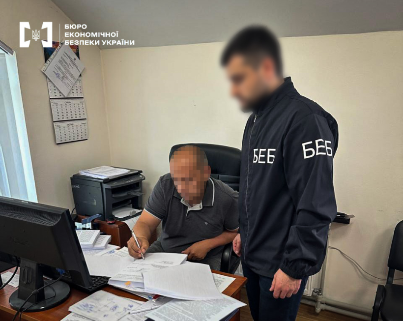 Оформлення процесуальних матеріалів у кабінеті: співробітник БЕБ стоїть поруч із громадянином, який заповнює папери