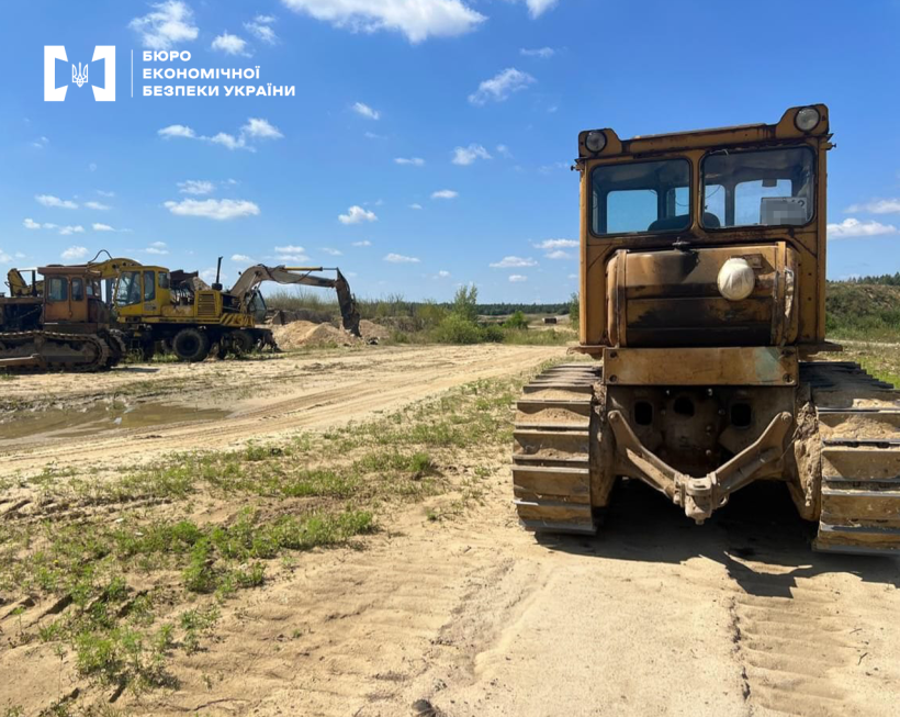 Бульдозер та екскаватор на відкритій місцевості серед піщаного ґрунту. На тлі блакитне небо з білими хмарами