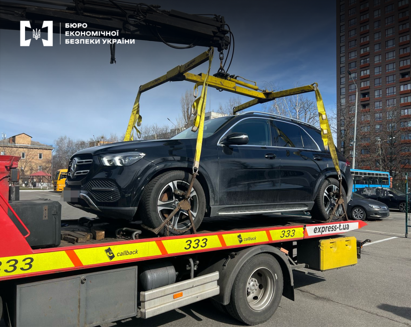 Завантаження автомобіля марки Mercedes-Benz за допомогою крана маніпулятора на причеп евакуатора. Вулиця міста, сонячний день, блакитне небо