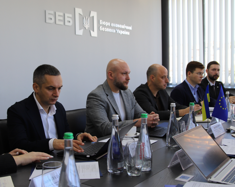 Leadership and staff of the Economic Security Bureau of Ukraine at the table against the wall with the logo and the inscription “Economic Security Bureau of Ukraine.”
