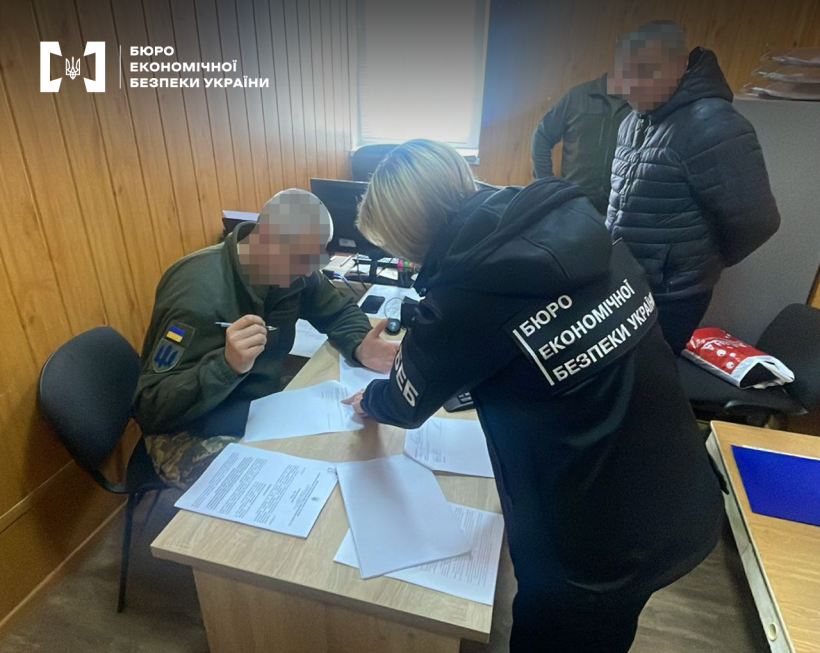 Жінка - детектив БЕБ ознайомлює з підозрою фігуранта справи. Позаду двоє чоловіків. Робочий кабінет, столи, комп’ютер.