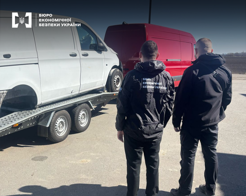 Детективи БЕБ проводять огляд транспортних засобів. На причепі червоного вантажного фургону стоїть білий автомобіль без заднього колеса.