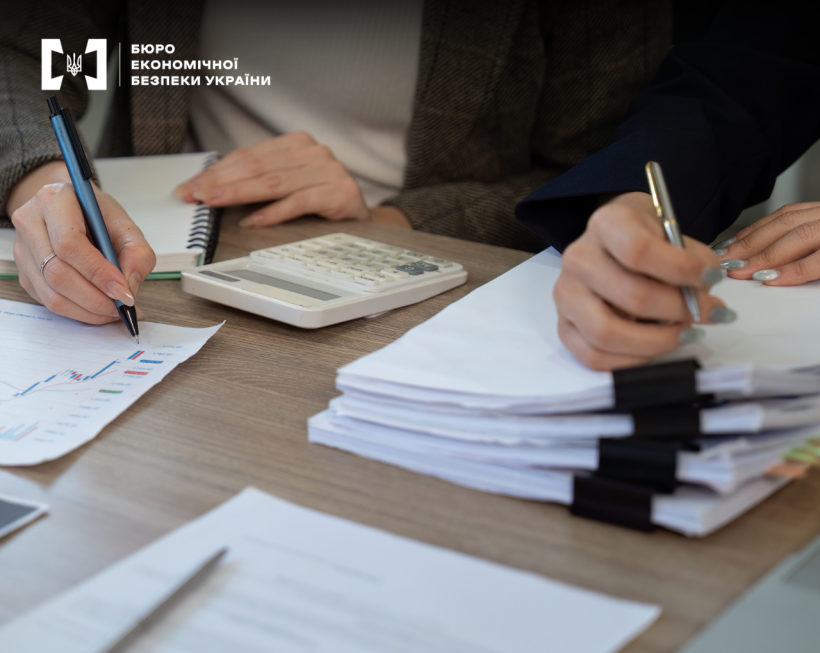 Руки двох людей, які працюють з фінансовою документацією. Калькулятор, графіки та стоси паперів на робочому столі.