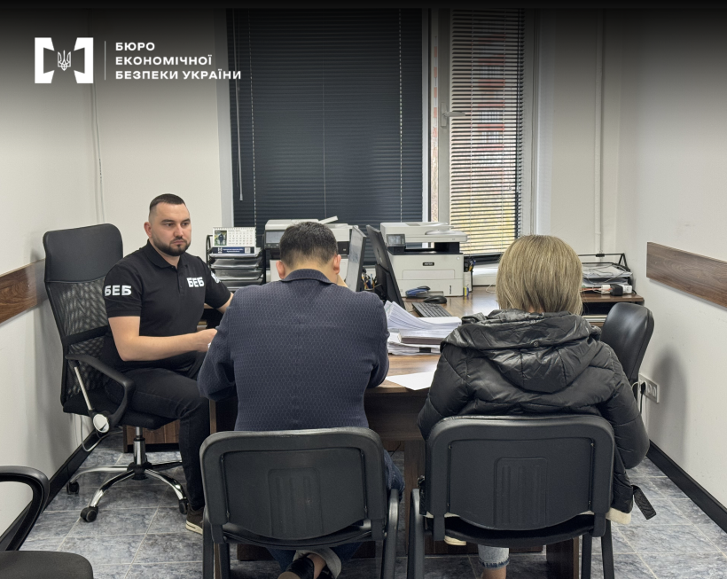 Investigative actions: a ESBU detective briefs the suspects in the case with documents at a work desk. View from behind the visitors' backs.