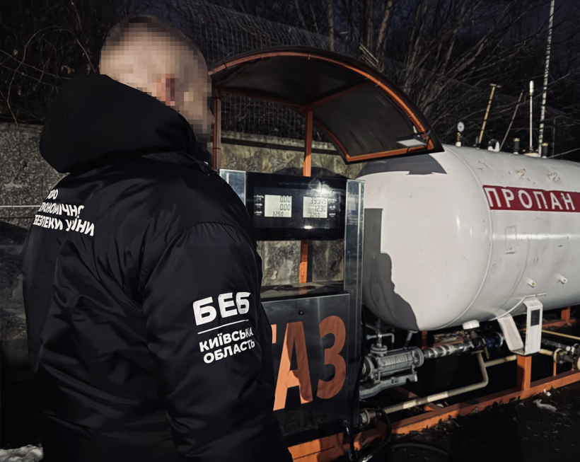 Детектив БЕБ оглядає паливороздавальну колонку з написом: «Газ», яка під’єднана до білого резервуару з написом: «Пропан». Темна пора доби.
