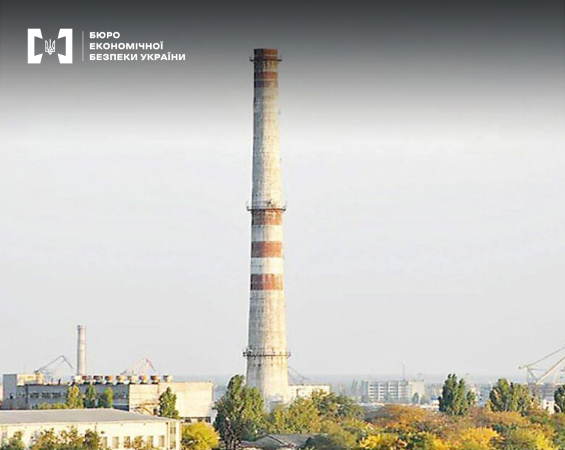 Труба Херсонської ТЕЦ з червоно-білими смугами на тлі міського пейзажу та похмурого неба.