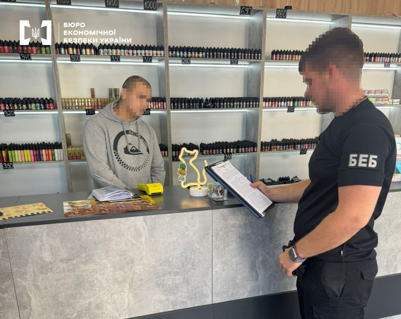 Детектив БЕБ у магазині з продажу тютюнових виробів. На полицях із цінниками електронні сигарети та рідини до них. За прилавком – чоловік.