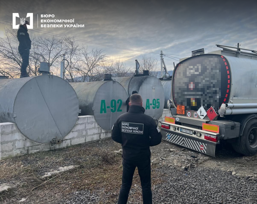 Два співробітники БЕБ оглядають паливні резервуари, два з яких марковано А-92, А-95, та бензовоз