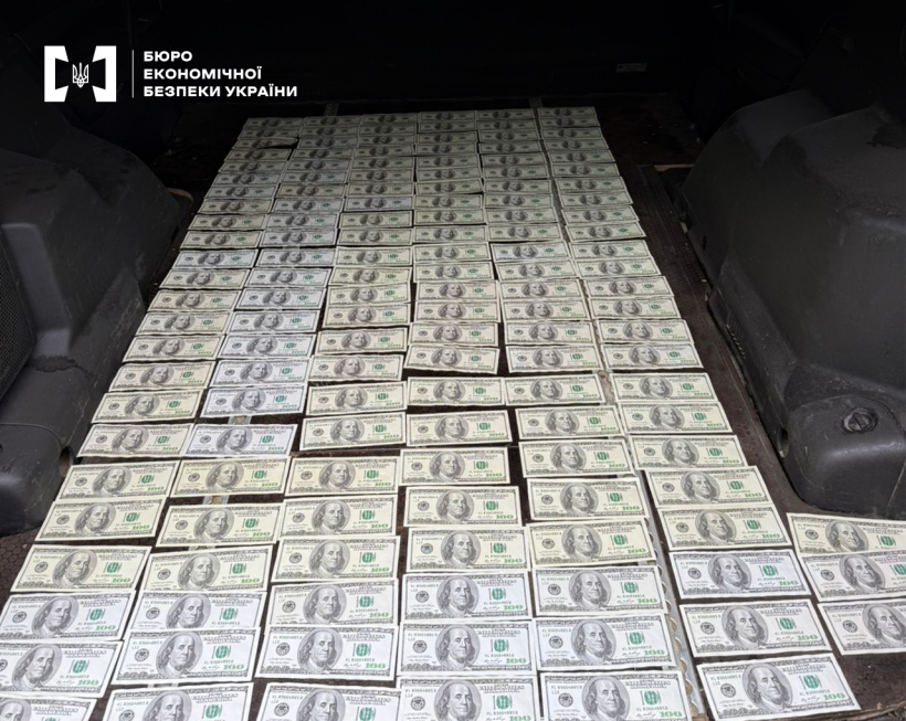 Банкноти номіналом 100 доларів США розкладені рядами у багажнику автомобіля.
