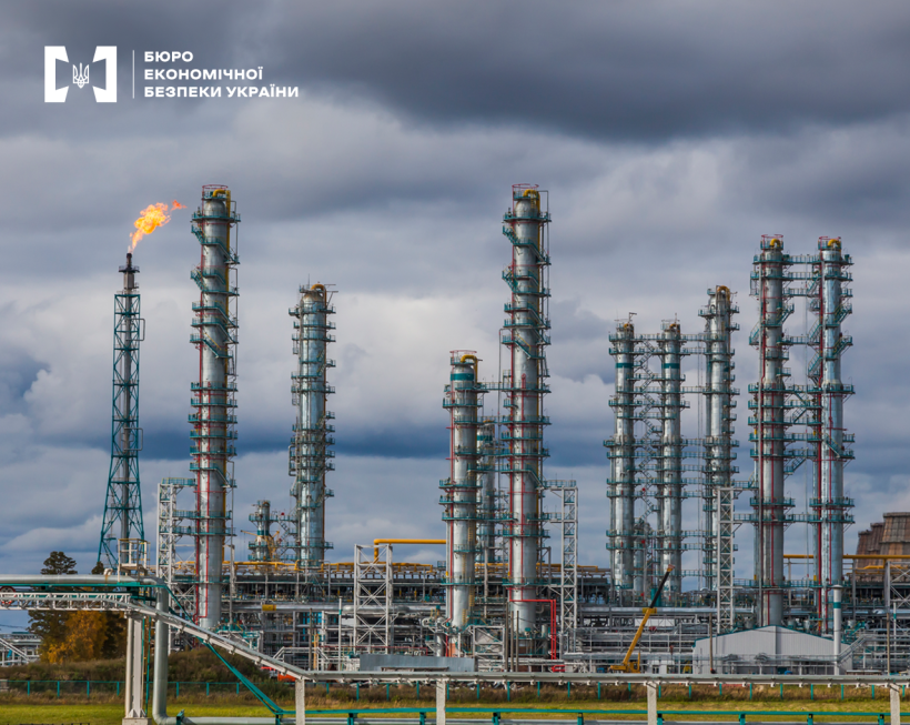 Вид здалеку на індустріальний комплекс з видобування природного газу. Високі колони, трубопроводи, факельна система. На тлі похмуре небо.