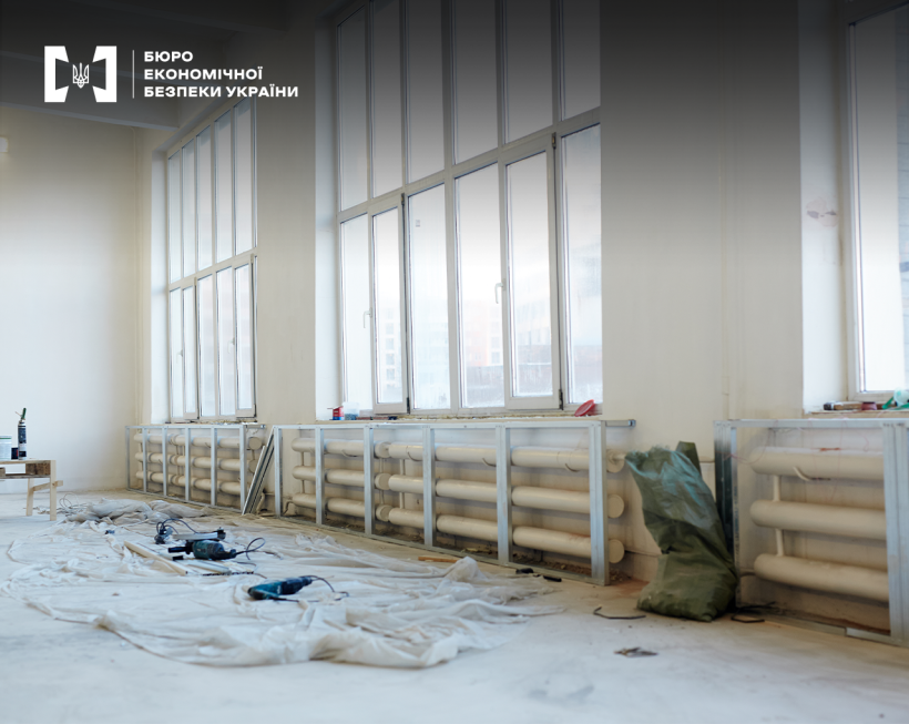 Світле приміщення з великими вікнами, уздовж стін встановлені нові батареї, на підлозі розкладені будівельні інструменти.