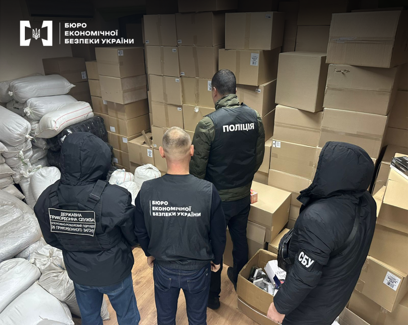 Працівники БЕБ, ДПСУ, СБУ та поліції оглядають склад, вщент заповнений картонними коробками та мішками з тютюном