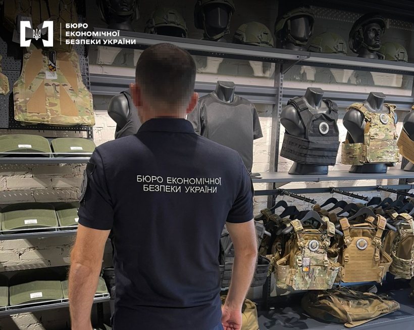 Детектив БЕБ проводить огляд вітрини з бронежелетами та шоломами у магазині військової амуніції.