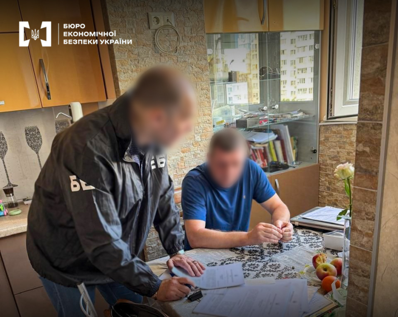 An ESBU detective reads out documents in front of a suspect in a blue t-shirt in a home environment.