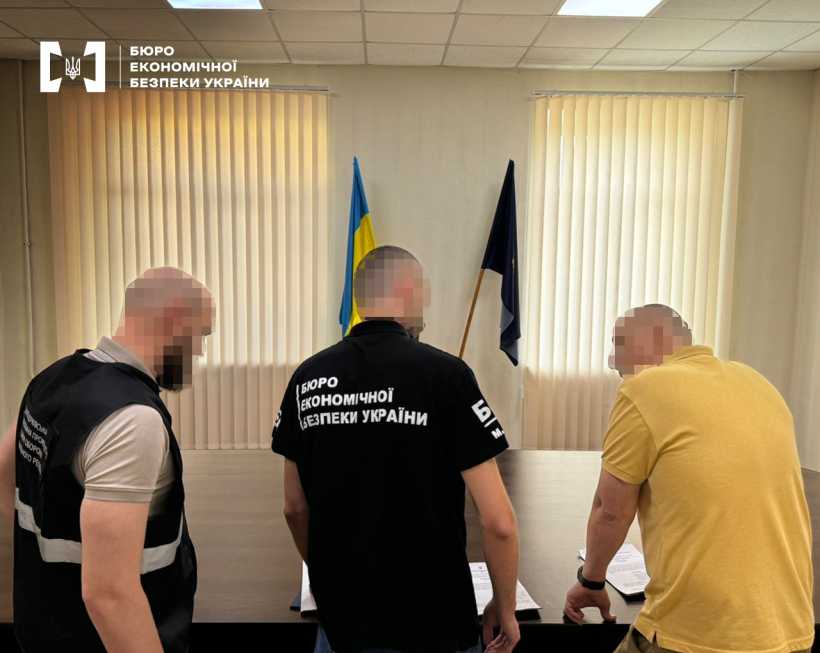 Просторий кабінет із державним прапором.  Детектив БЕБ оголошує підозру фігуранту справи. Поруч працівник прокуратури.