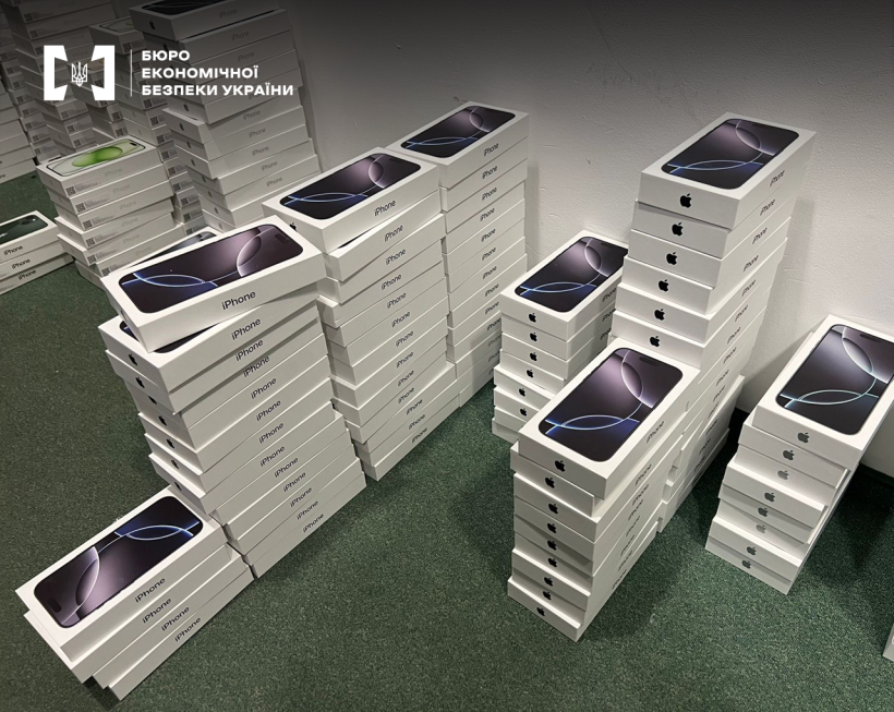 Смартфони у білих коробках у великій кількості розкладені стовпчиками у ряди на зеленій підлозі.