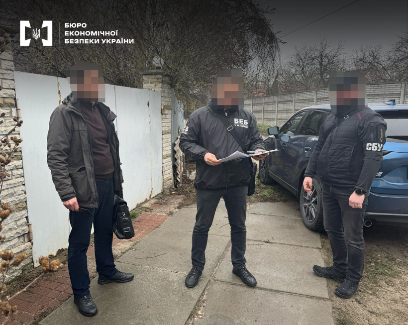 Працівники БЕБ і СБУ оголошують підозру фігуранту справи. Приватний сектор, вулиця, залізні ворота, припаркована автівка, паркан, за ним верхівки дерев.