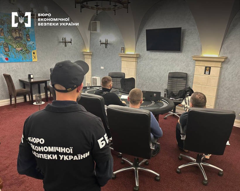 Детектив БЕБ та ще троє чоловіків у підпільному казино. Просторий зал з сірими стінами та колонами, червоною підлогою. Стіл для гри у покер, крісла.