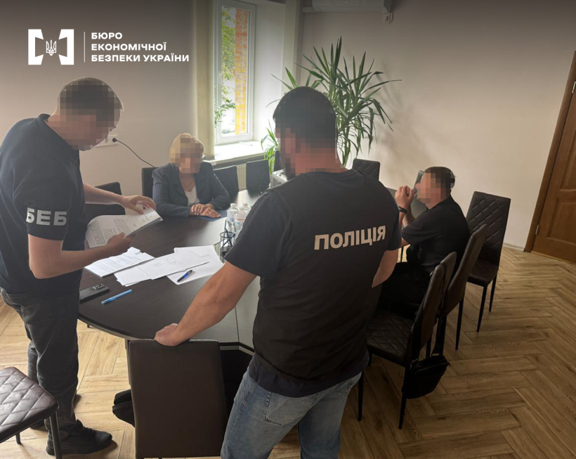 Офісне приміщення. Працівники БЕБ та поліції ознайомлюються з документами. За столом сидять жінка і чоловік.