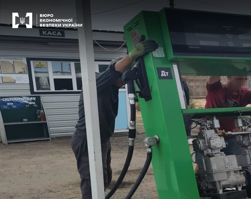 Територія автозаправної станції. Двоє чоловіків демонтують зелену паливну колонку АЗС.
