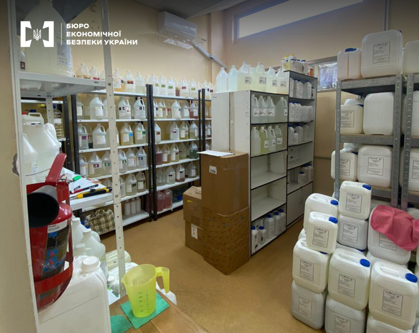 Складське приміщення, заповнене стелажами. Велика кількість ємностей та каністр з рідинами на стелажах та підлозі.