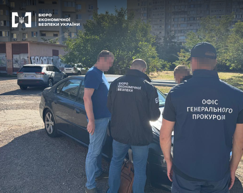 Детектив БЕБ та працівник прокуратури вручають підозру фігуранту справи біля припаркованого на міській вулиці автомобіля.