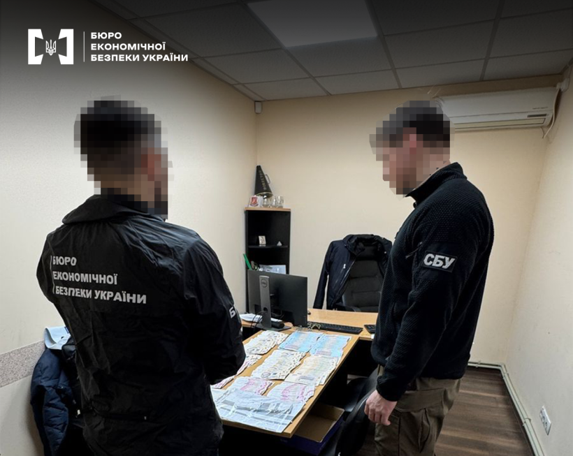Двоє працівників БЕБ та СБУ проводять вилучення доказів в офісі. На столі гроші, розкладені за номіналами та документи