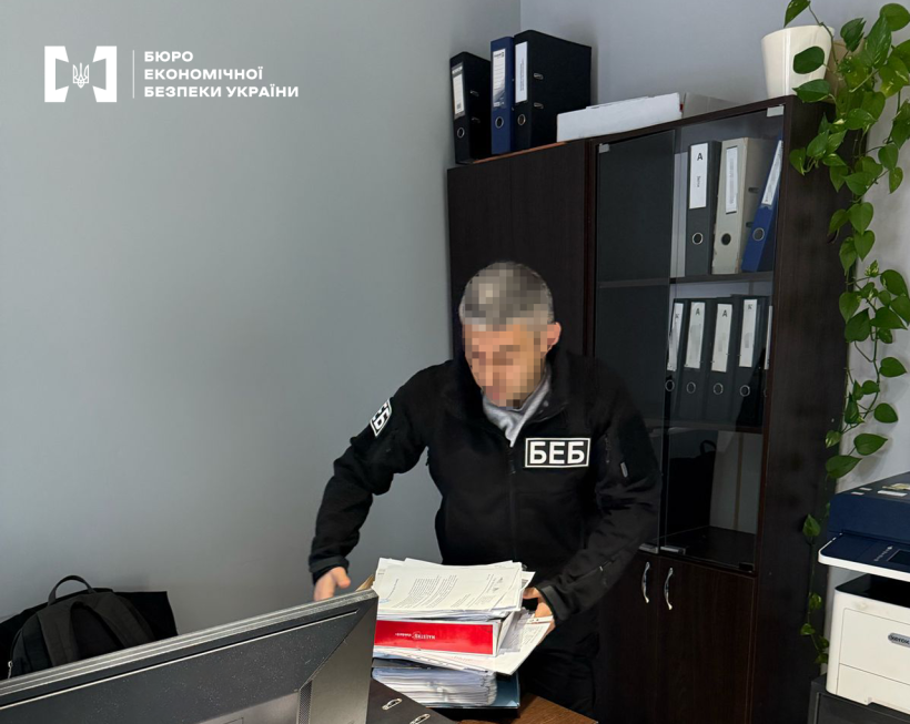 Детектив БЕБ вилучає документи в офісі. Лице заблорене. Шафа для документів, офісна техніка