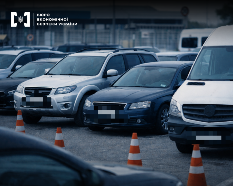 Легкові автомобілі та мікроавтобуси, що стоять щільними рядами на майданчику. Перед ними помаранчеві дорожні конуси зі світловідбивними смугами.