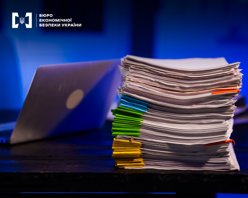 Стос документів та відкритий ноутбук на столі на фоні кольору синій електрик.