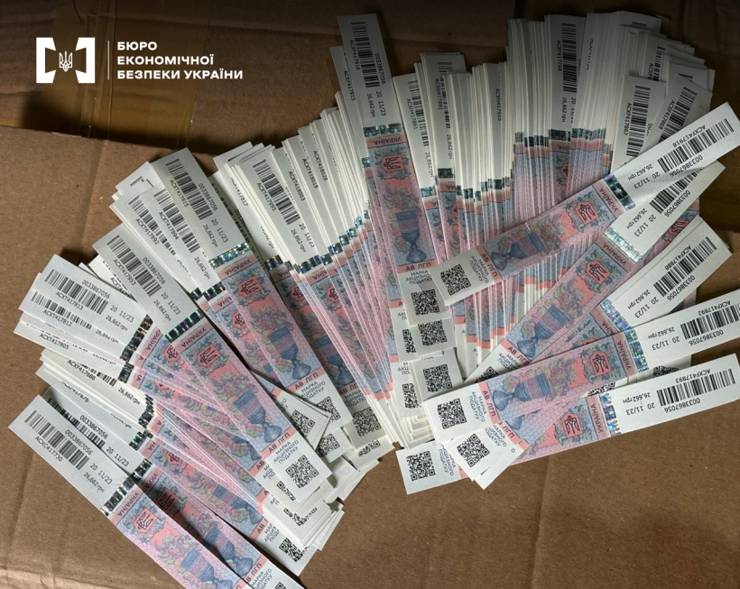Велика кількість підроблених акцизних марок з голограмами та QR-кодами розкладені на картонній коробці.