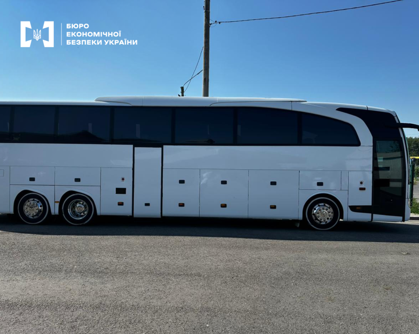 Білий автобус припаркований на узбіччі дороги. Над ним — блакитне небо без жодної хмаринки.