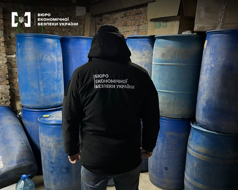 Детектив БЕБ оглядає приміщення з металевими синіми бочками, що складені одна на одну