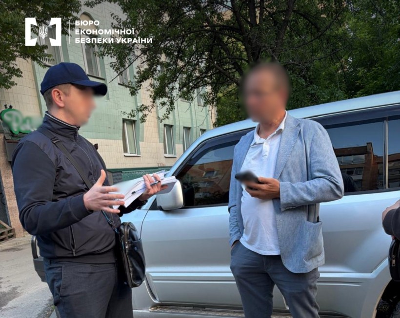 Детектив БЕБ спілкується з чоловіком у блакитному піджаку з документами на вулиці біля сріблястого позашляховика