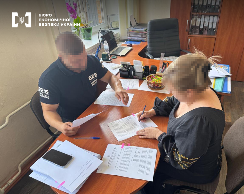 Повідомлення про підозру фігурантки справи. Детектив БЕБ та жінка сидять за столом у робочому кабінеті. Жінка підписує документи.