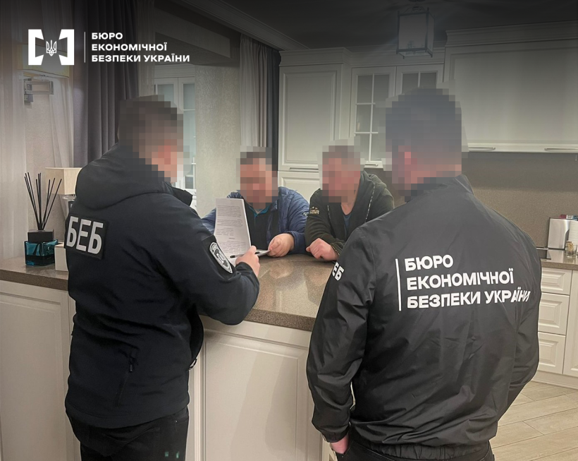 Два детективи БЕБ зачитують протокол обшуку двом чоловікам. Всі обличчя заблюрено.