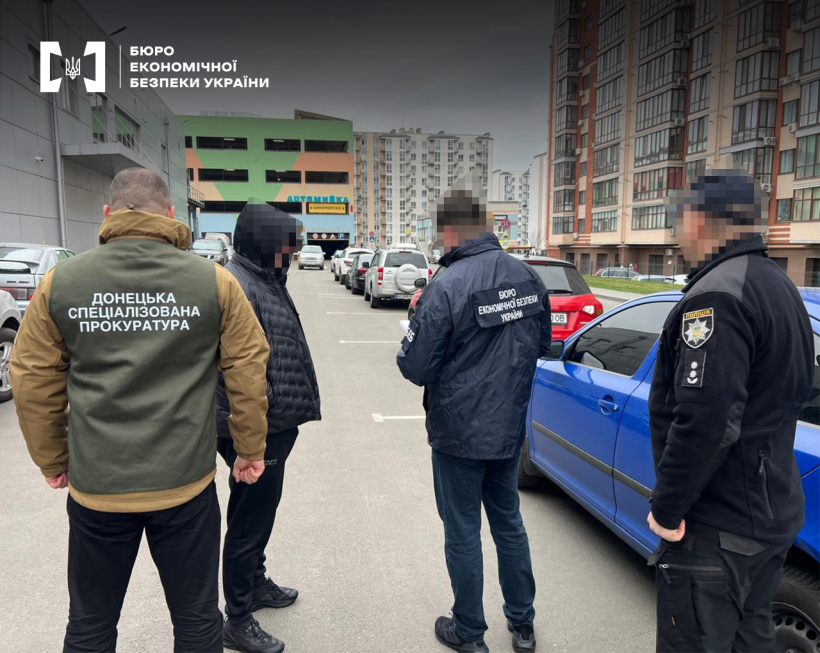Працівники БЕБ, Донецької спеціалізованої прокуратури і поліції оголошують підозру одному з фігурантів справи на парковці ТРЦ. Поруч багатоповерхівки