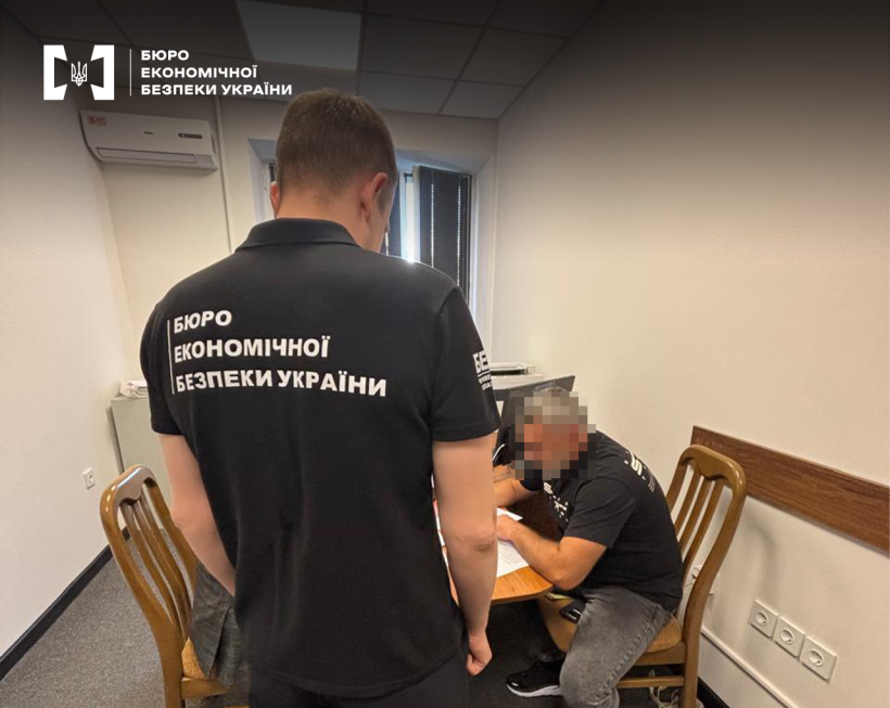 Чоловік за столом у робочому кабінеті ознайомлюється з документами. Поруч стоїть детектив БЕБ.