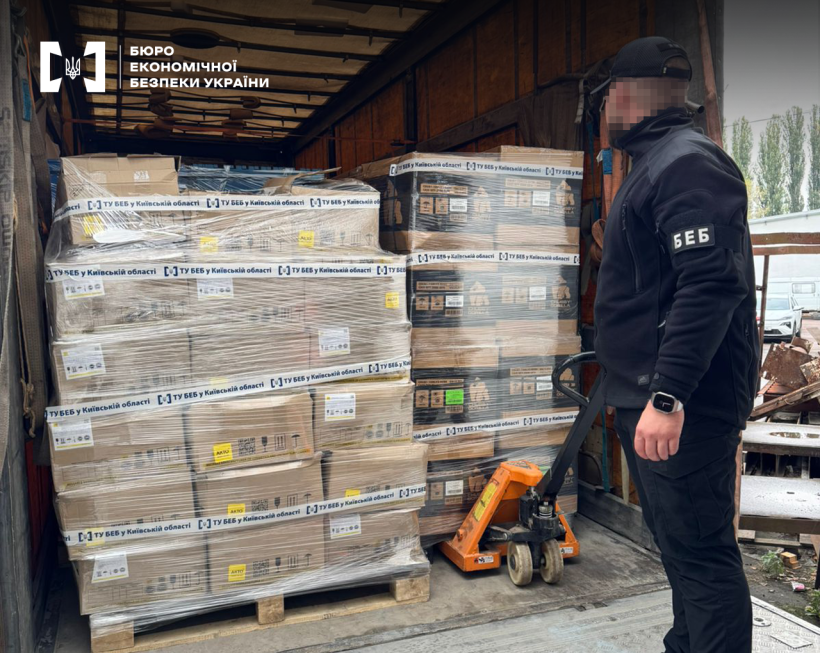 Детектив БЕБ оглядає коробки у фургоні на палетах, обмотані стрейч-плівкою та заклеєні скотчем з логотипом БЕБ та написом «ТУ БЕБ у Київській області»
