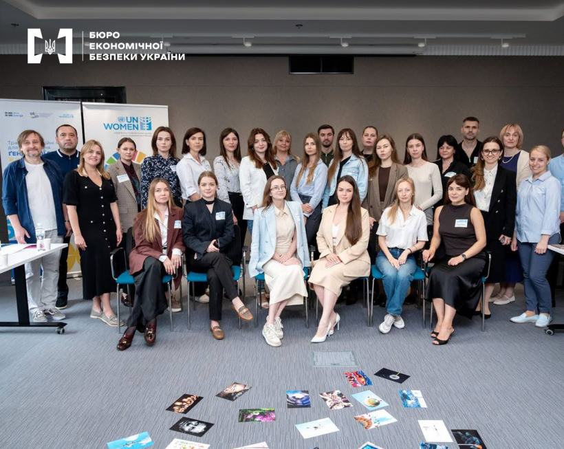 Group photo of event participants, with colourful cards and brochures scattered on the grey floor in front of them.