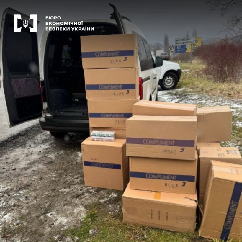 Коробки з контрафактними сигаретами біля відкритого багажника автомобіля, що стоїть обабіч дороги. Дерева, кущі, дорожні знаки.