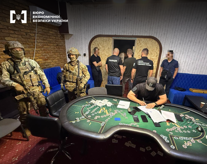 Обшук у підпільному казино. Серед залу стіл для гри у покер, на ньому документи, смартфони. Біля столу працівники БЕБ, Національної поліції та казино.