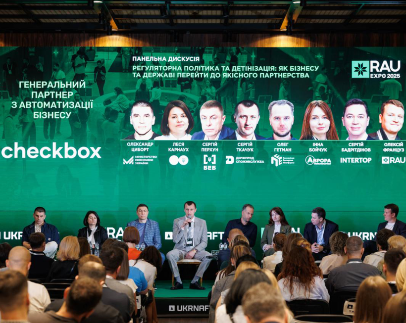 Спікери панельної дискусії на фоні банера з їхніми фотографіями, іменами та прізвищами, посадами, назвою заходу у конференц-залі.