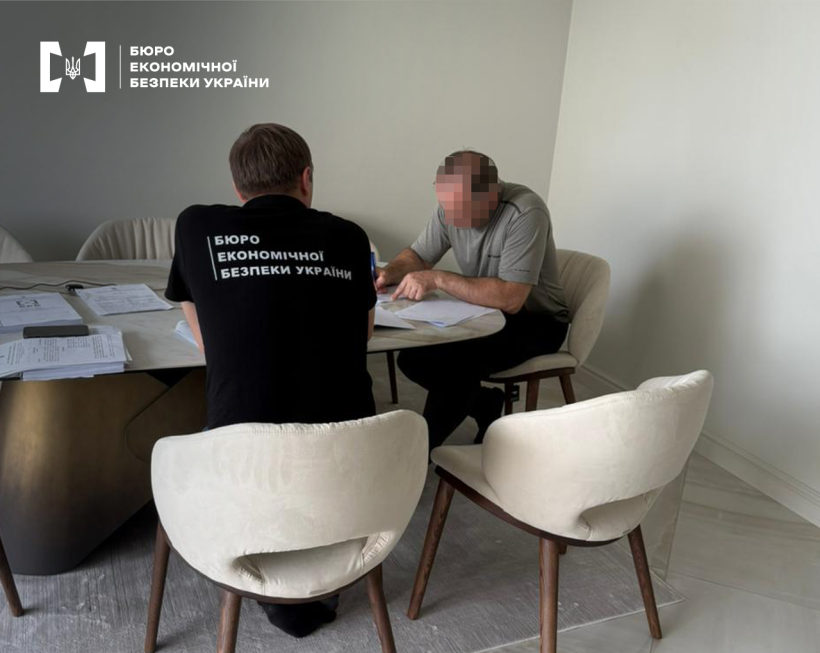 Офісне приміщення. Детектив БЕБ вручає підозру фігуранту справи за круглим столом з паперами та документами.