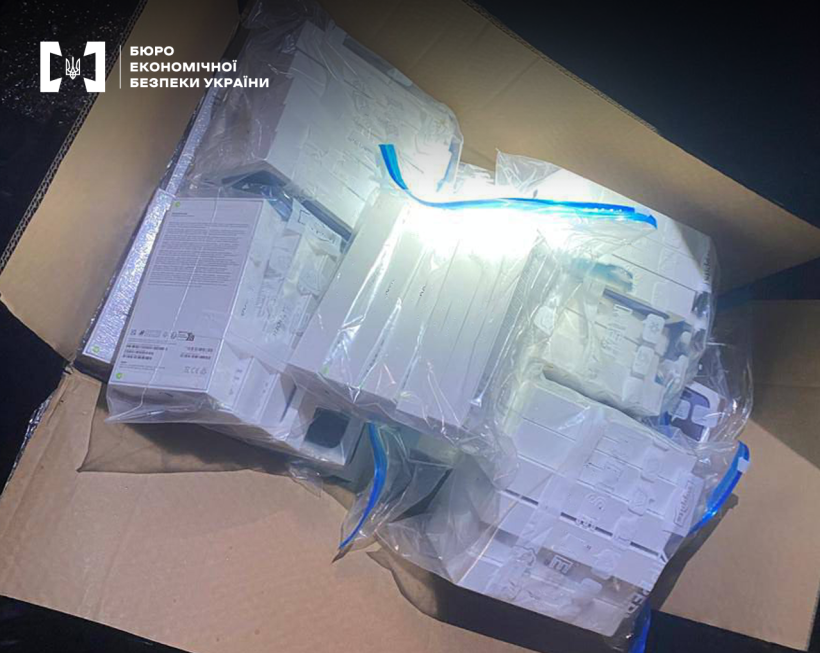 Мобільні телефони в упаковці, складені по кілька штук у прозорі пакети, у відкритій картонній коробці.